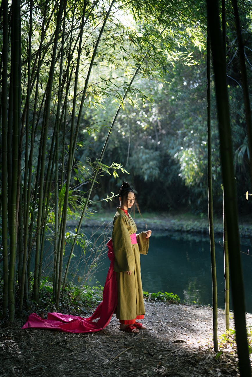 woman in green kimono standing near green bamboo trees